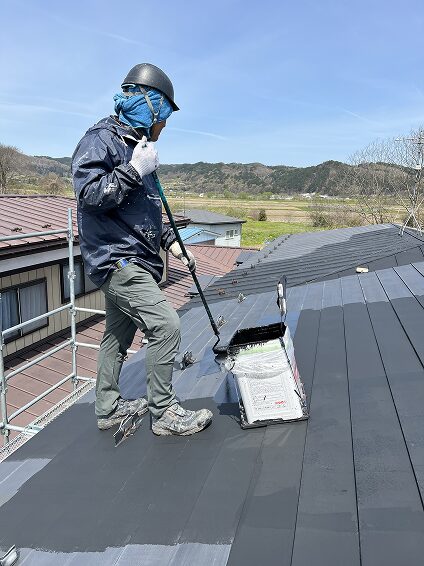 屋根の上でローラーを使って塗装作業を行う椛沢Prime塗装の職人